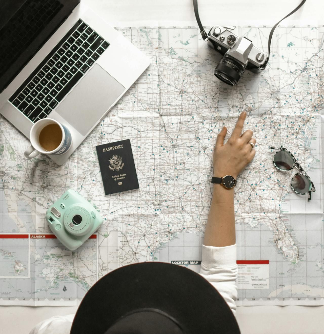 person plotting holidays or travel on a map with passport, camera and coffee